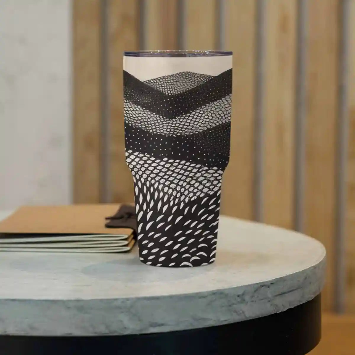 Mountains digital art print on a 30 oz travel mug placed on a concrete table, featuring abstract black and white rolling hills.