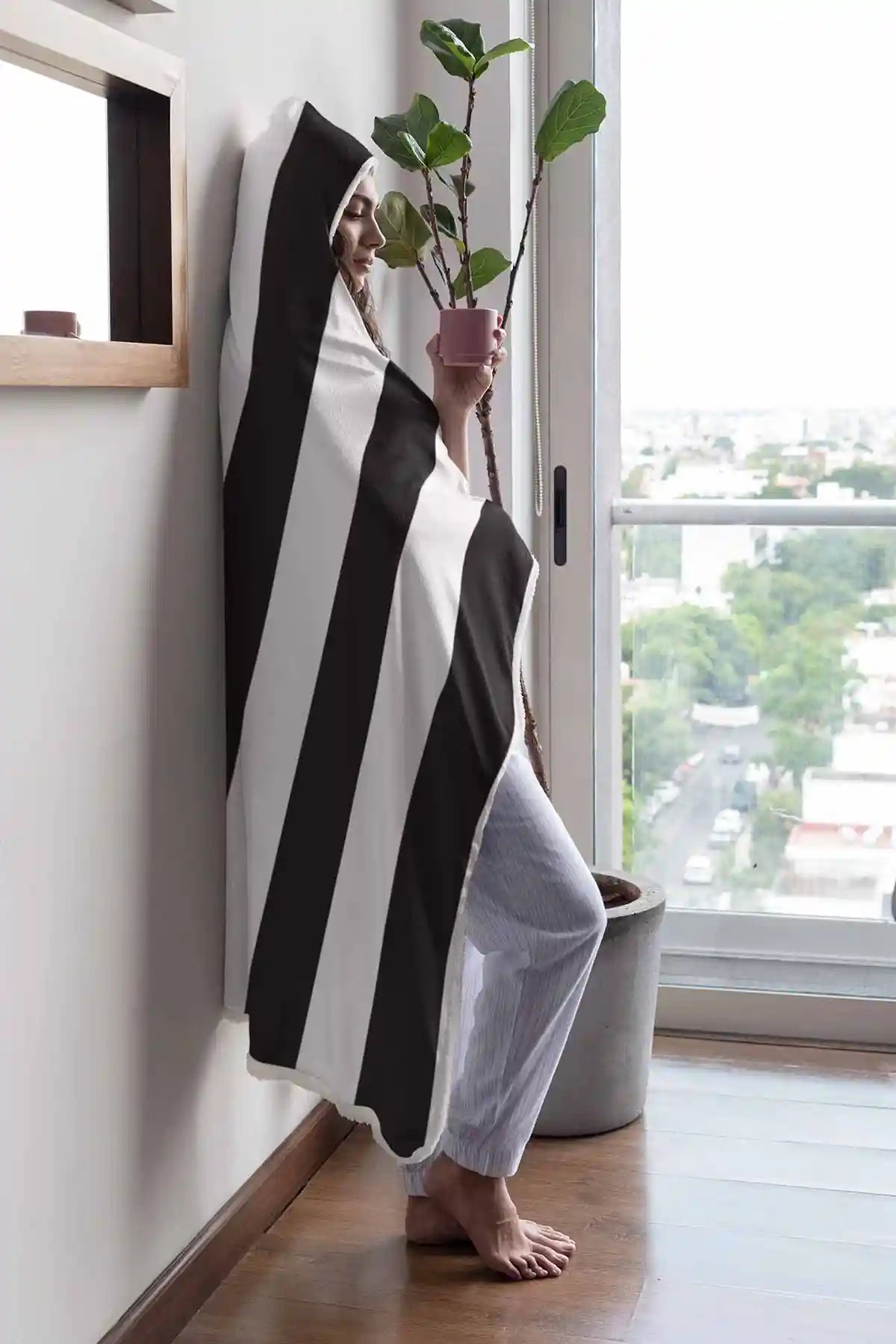 Vertical Stripes digital art printed on a hooded fleece blanket, featuring a woman drinking coffee, with bold black and white diagonal lines, adding a touch of modern abstraction and comfort to the space.